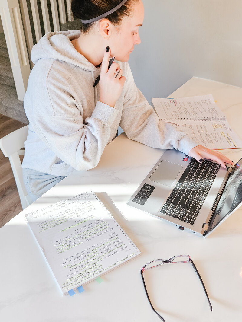 girl working on laptop on counter holding hand to face