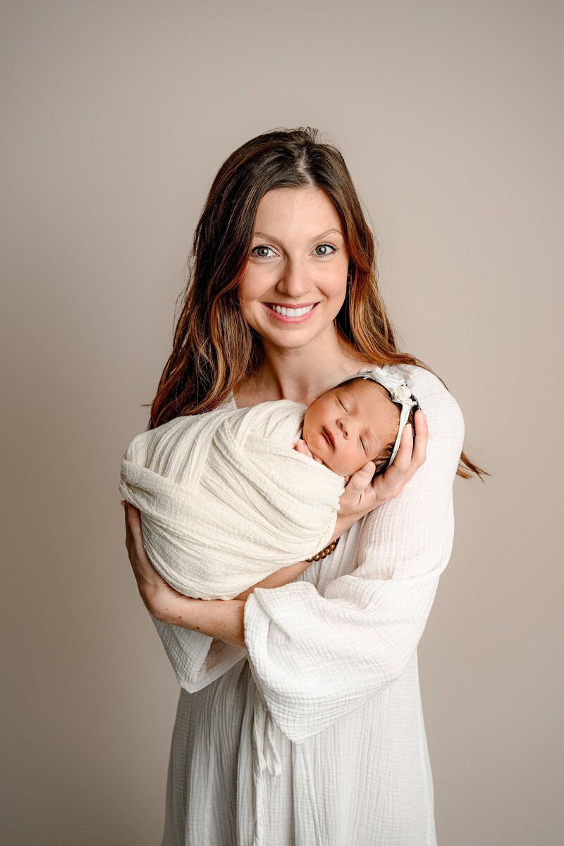 mother holds her newborn daughter while both are dressed in cream