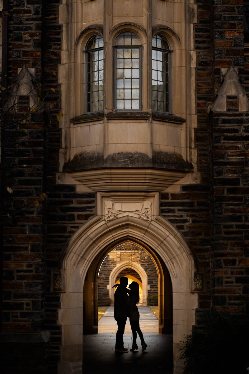 Silhouetted couple standing under an arched doorway of a Gothic stone building with a warm light glowing from the background