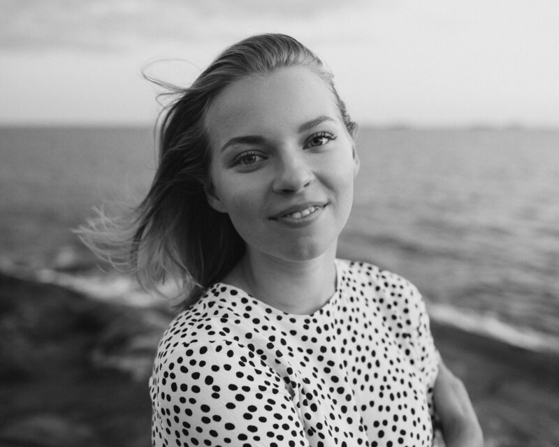 Nainen hymyilee hennosti kameralle rantakalliolla Suomenlinnassa Helsingissä