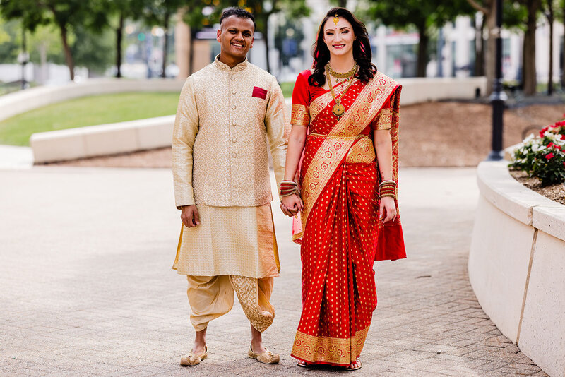 A bride and groom standing outside holding hands and smiling