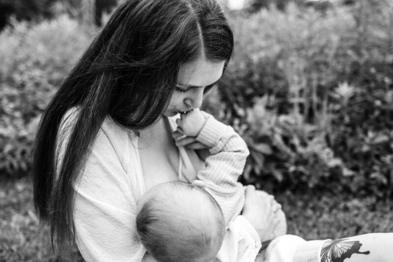 Black and white photo of woman nursing a baby and kissing baby's hand.