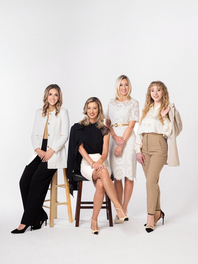 The four-person team of Emily Coyne Events poses in business attire and  smiles calmly against a white background.