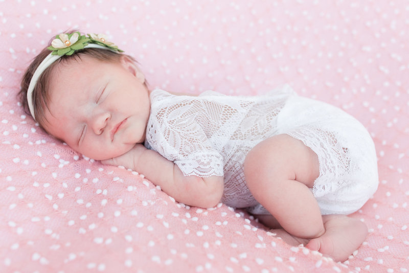 Newborn baby girl sleeps atop a pink and white speckled coverlet during newborn photography session