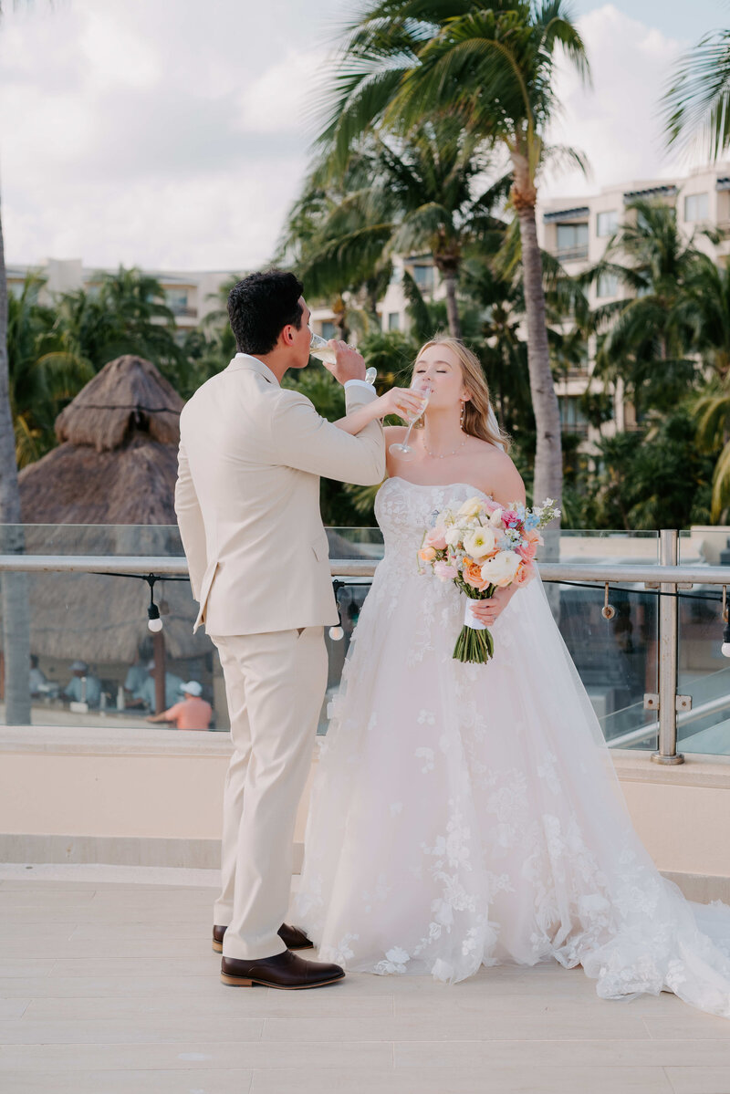 Romantic tropical wedding moment of a bride and groom sipping champagne together on a balcony