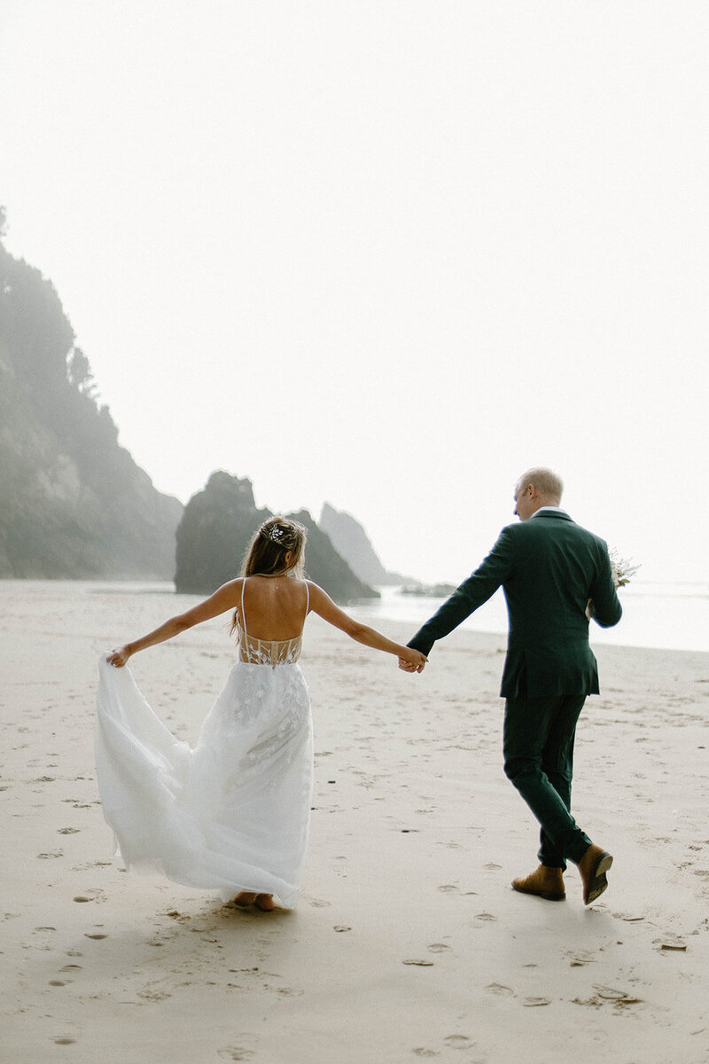 Bride and groom hold hands as they walk down Cannon Beach during their elopement.
