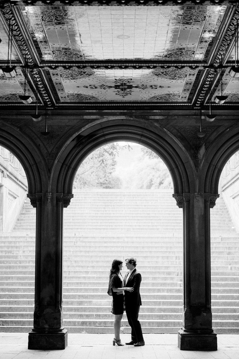 Couple stands in archway in Central park for best Central Park engagement photos