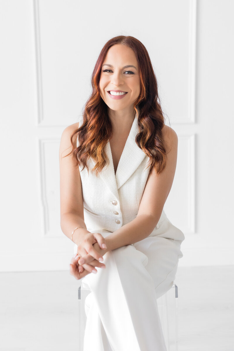 Bio photo of Florida wedding photographer, Angelika Krug sitting on a chair in a natural light studio.