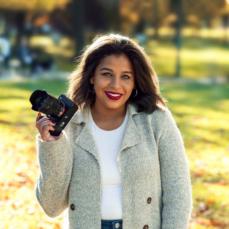 A latina woman holding a camera and smiling at the camera.