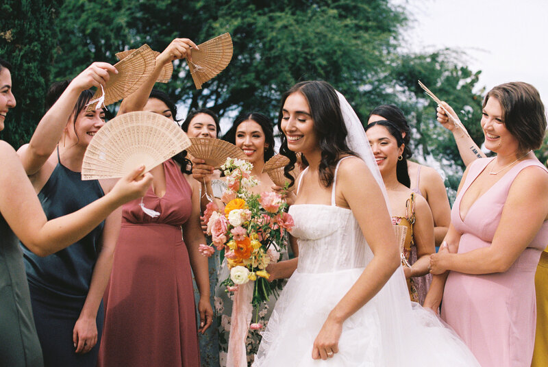 Bride with wedding bouquet surrounded by bridemaids with wooden fans