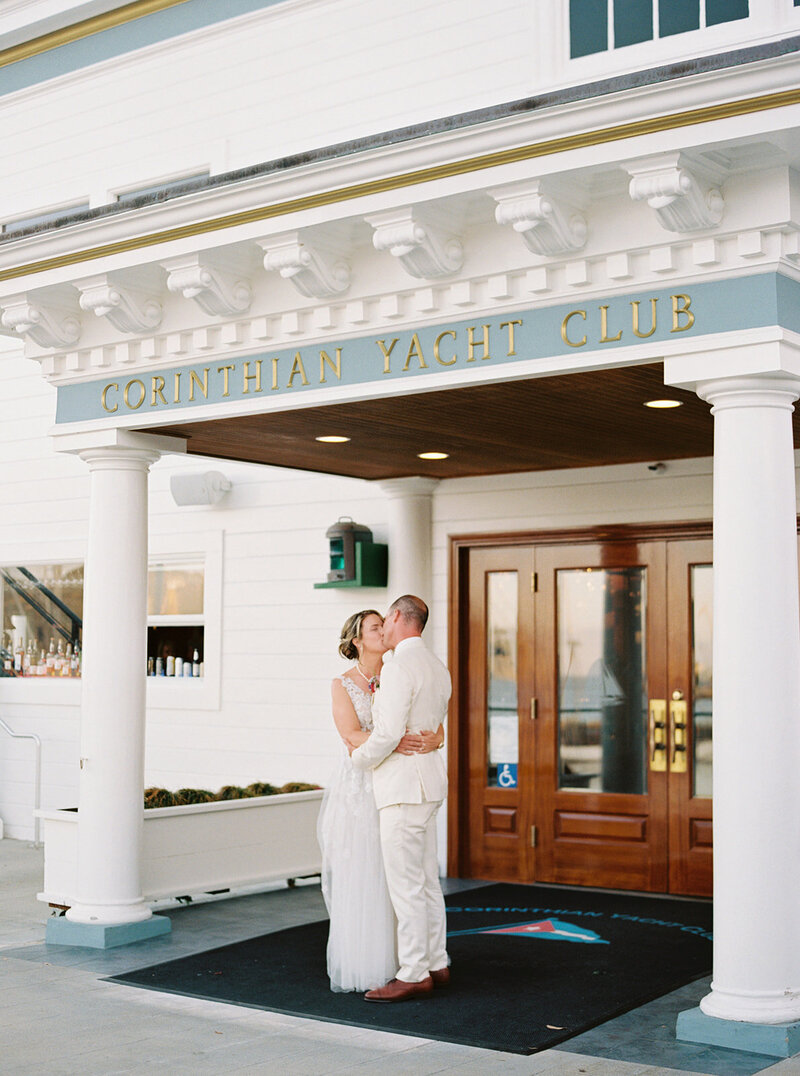 Bride and groom share a kiss beneath the classic architecture of the Corinthian Yacht Club in Tiburon, CA, photographed in luxury editorial style.