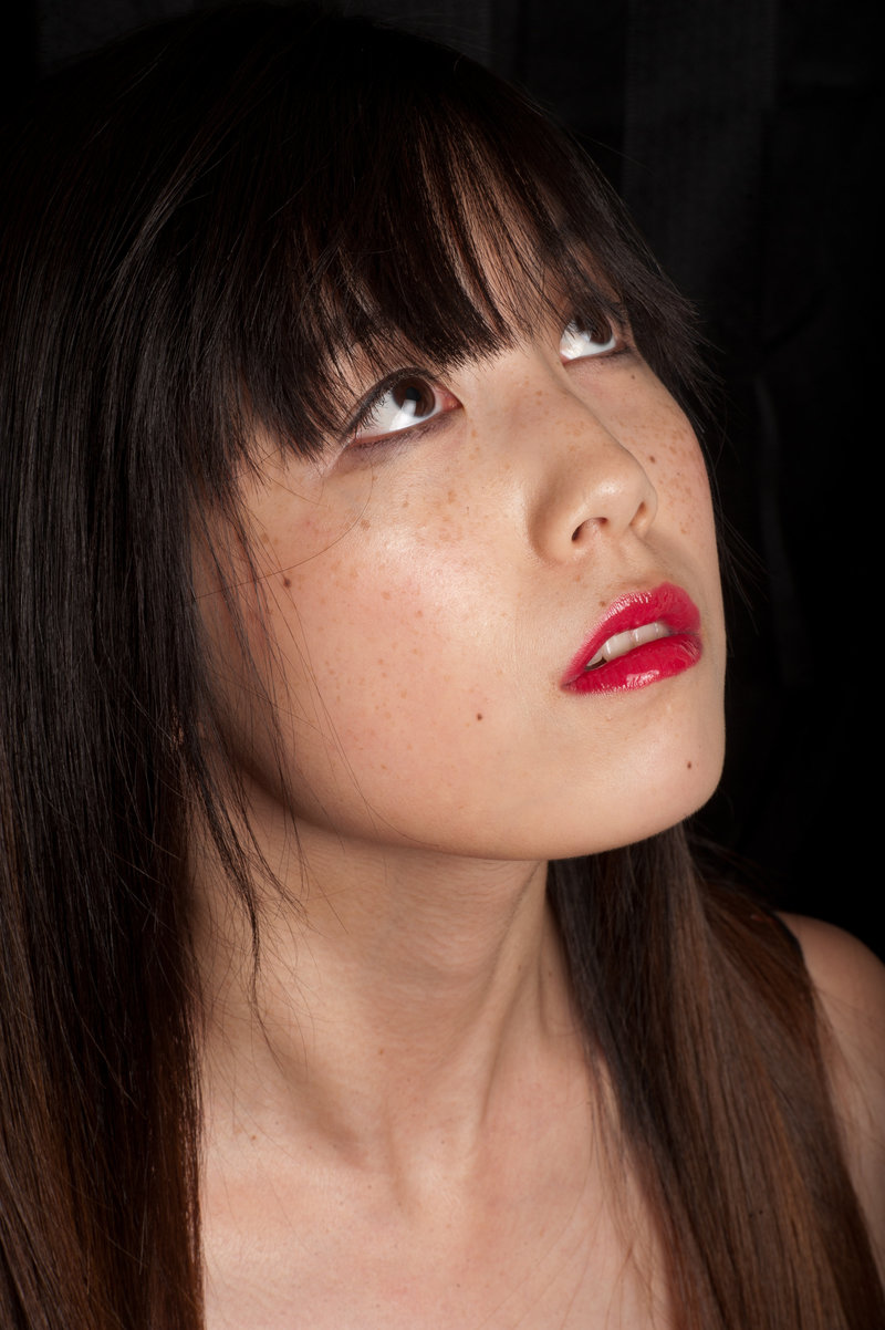 Asian beauty with black liner, lashes and red glossy lips with super clean looking skin showing her freckles