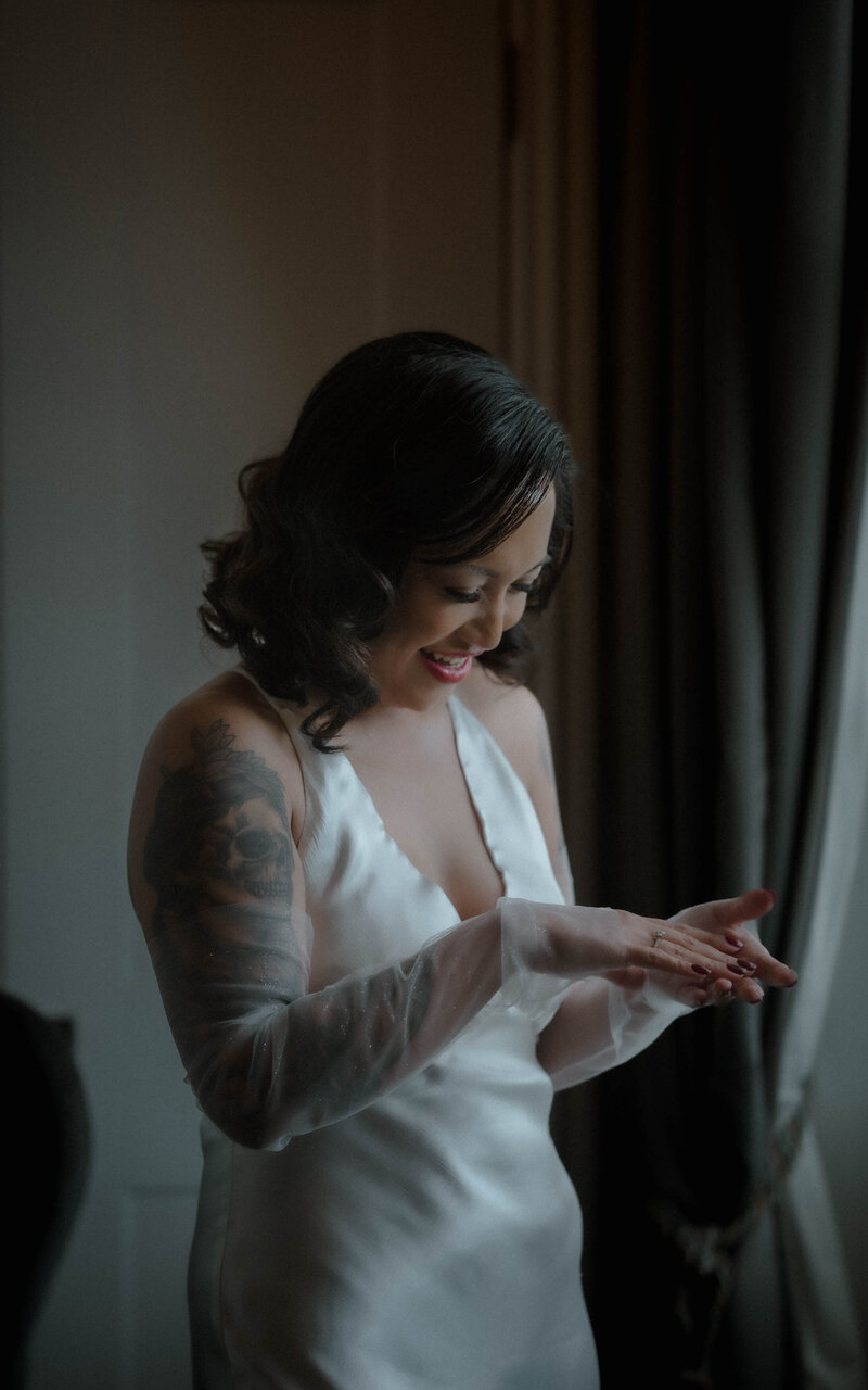 Bride standing next to the window, bathed in soft natural light, capturing a serene and elegant moment as she prepares for her wedding day, radiating beauty and grace