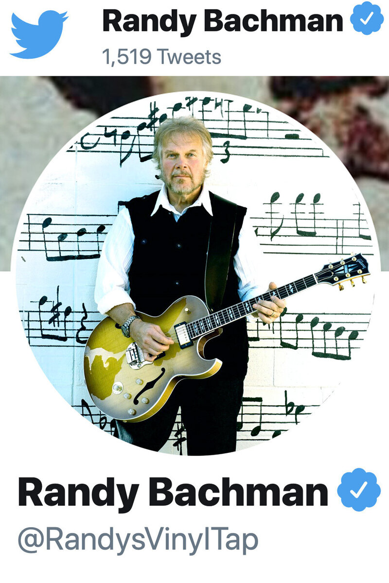 Randy Bachman Twitter profile photo standing in front of wall with musical notes painted on it holding guitar