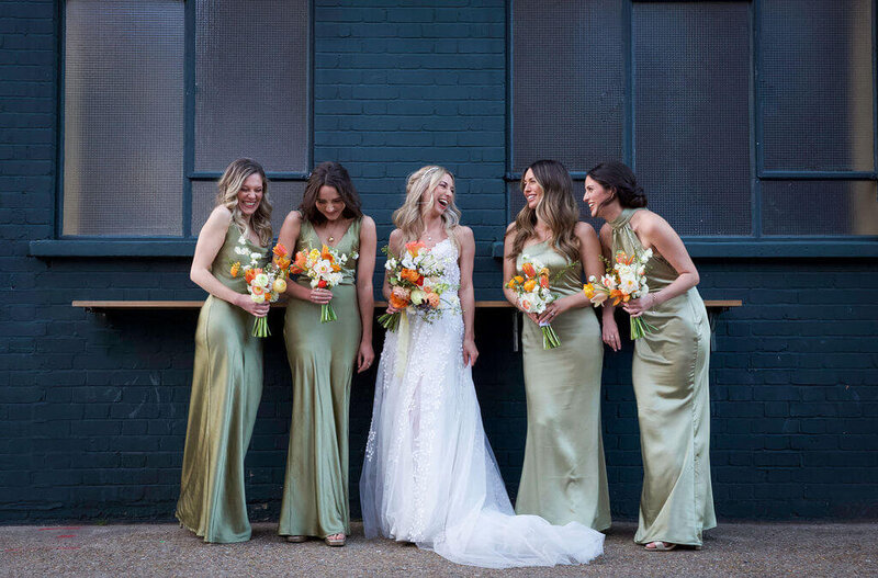 Bride is laughing to her four bridesmaids.  Bride and bridesmaids are leaning against wall of Mama Shelter Shoreditch