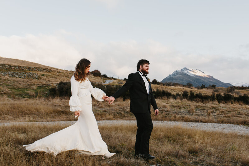 The Lovers Elopement Co - bride and groom walk through Queenstown mountains