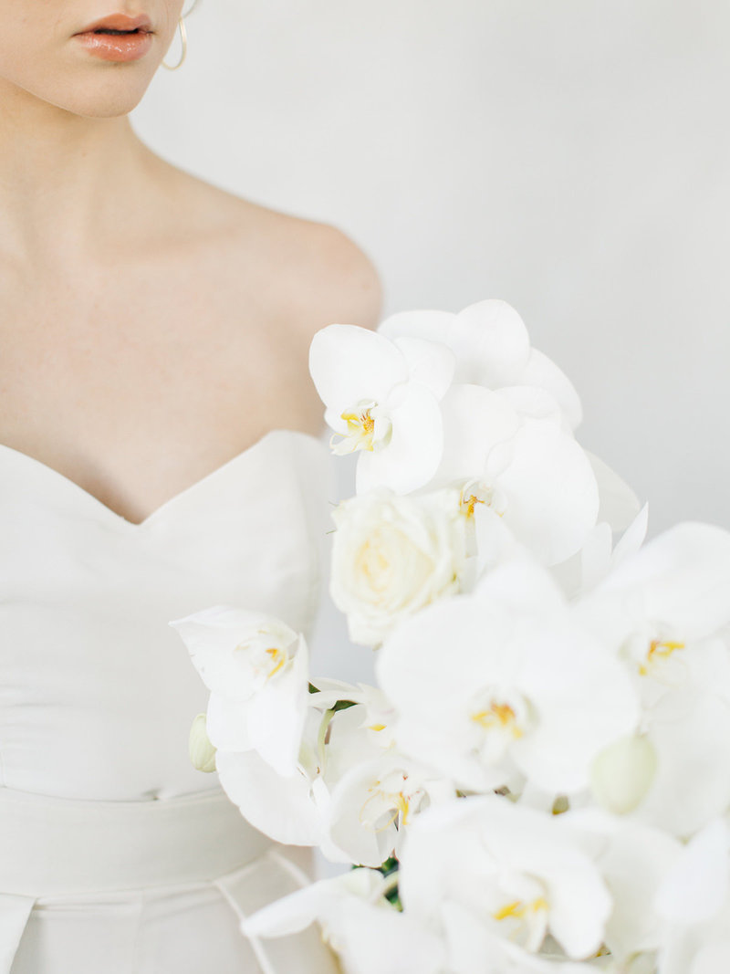 bride wearing pant suit with cape wedding dress holding an all white orchid bouquet