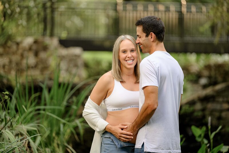 father whispers in mothers ear to make her laugh while they both touch her pregnant belly