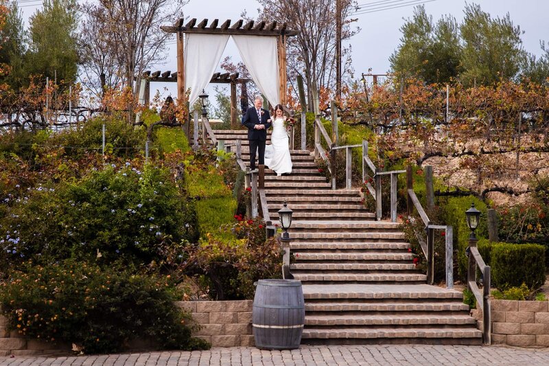 A bride and her father descending the grand staircase at her wedding ceremony at Lake Oak Meadows venue in Temecula.