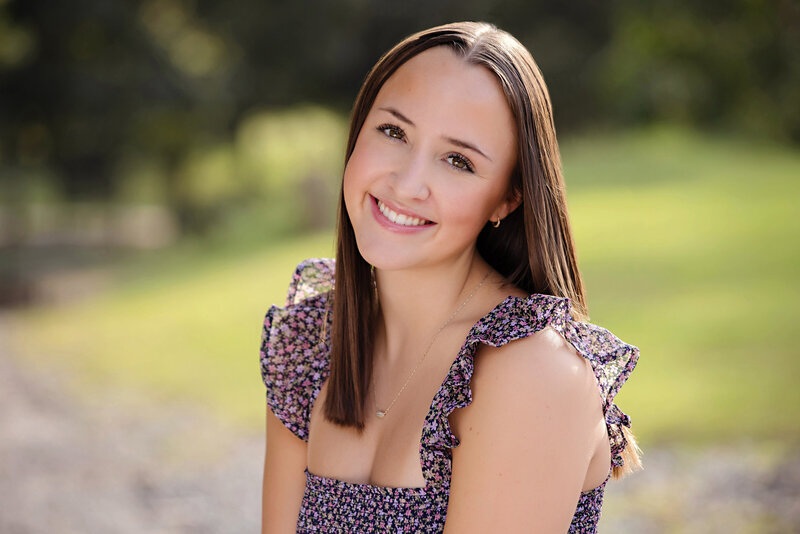 Close-up portrait on a HS Senior with a sleeveless dress with ruffles on the straps looking straight at the camera and smiling.