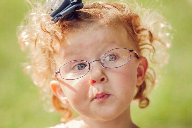 Close up of a little girl with curly, red hair, making a sweet face and looking off to the side.