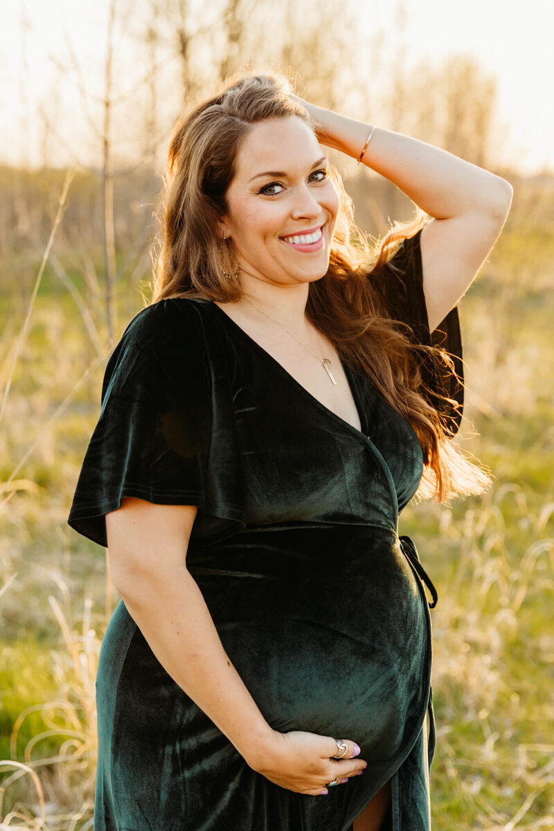 beautiful pregnant woman holding her hair back while wearing a velvet dress by Ashley Kalbus Photography