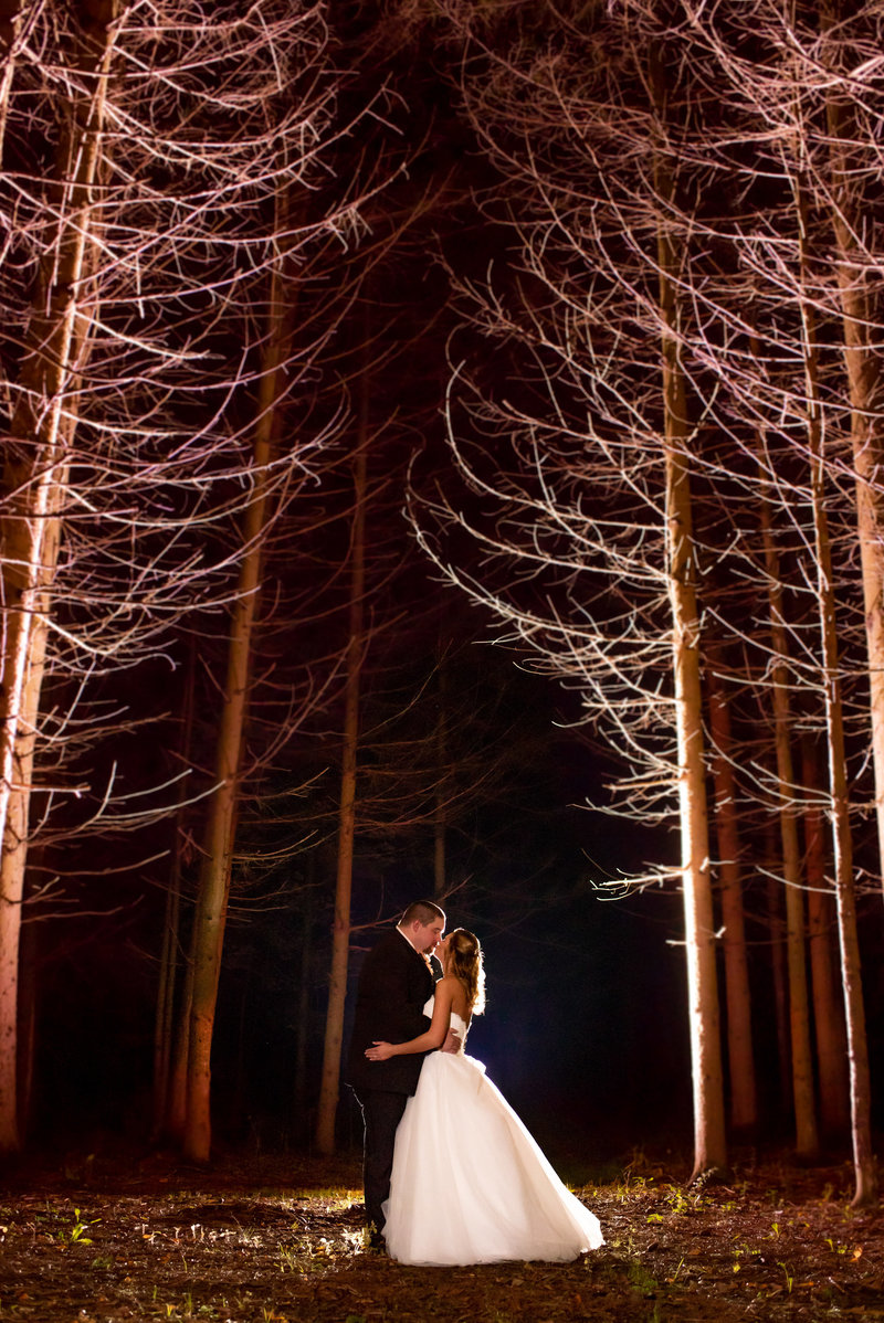 Night time photo of bride and groom kissing among tall pine trees