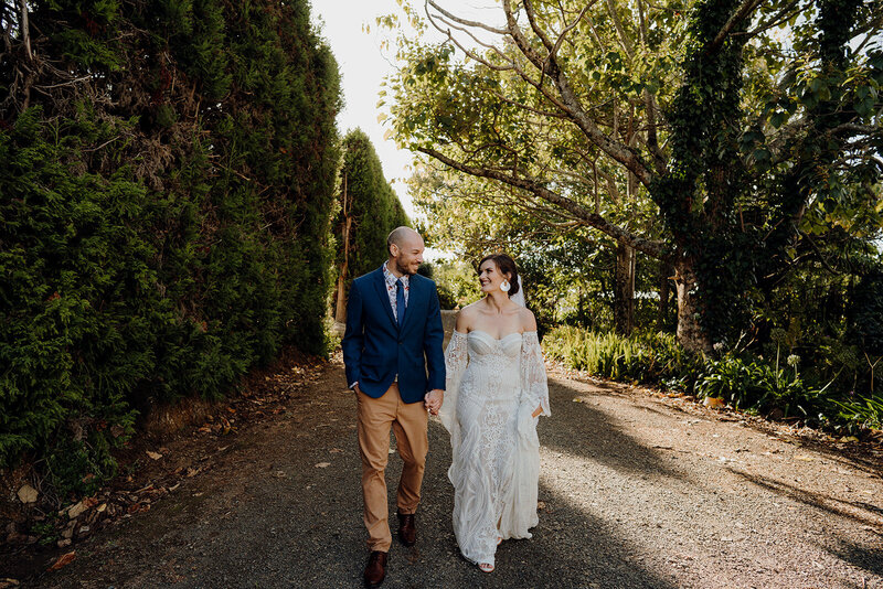 A boho bride and groom walking in the trees at Liddington Gardens during a wedding photoshoot with Haley Adele Photography