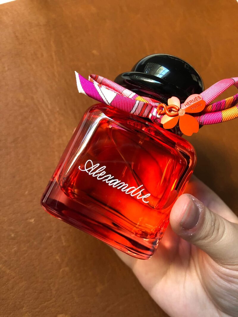Hand holding up a red perfume bottle with engraved name Alexandre