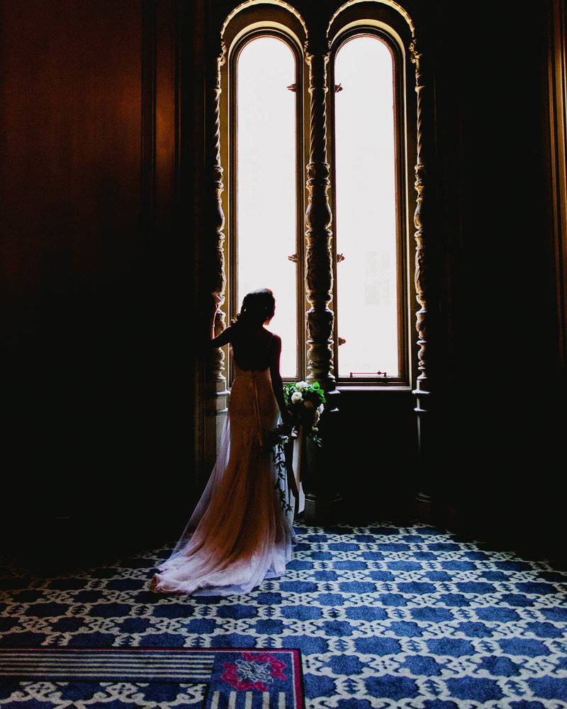 Bride silhouette in dress  holding bouquet in front of two big windows