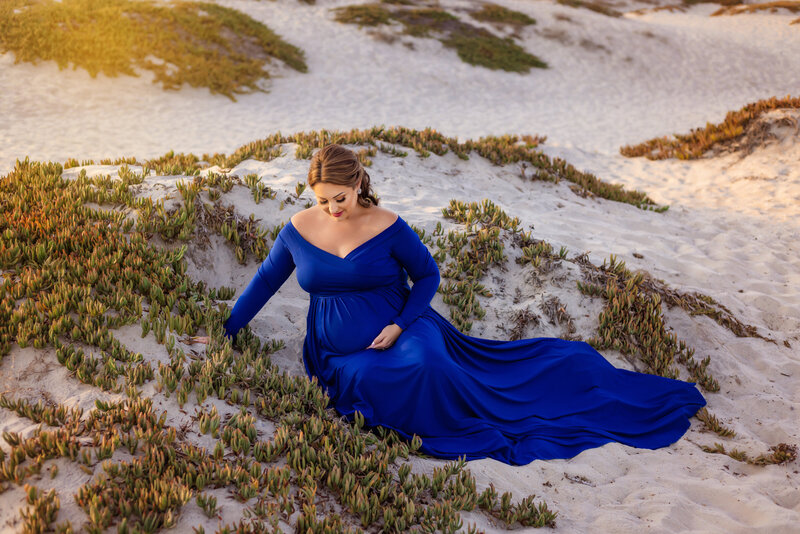 Maternity Photographer, a pregnant woman sits on a sandy beach