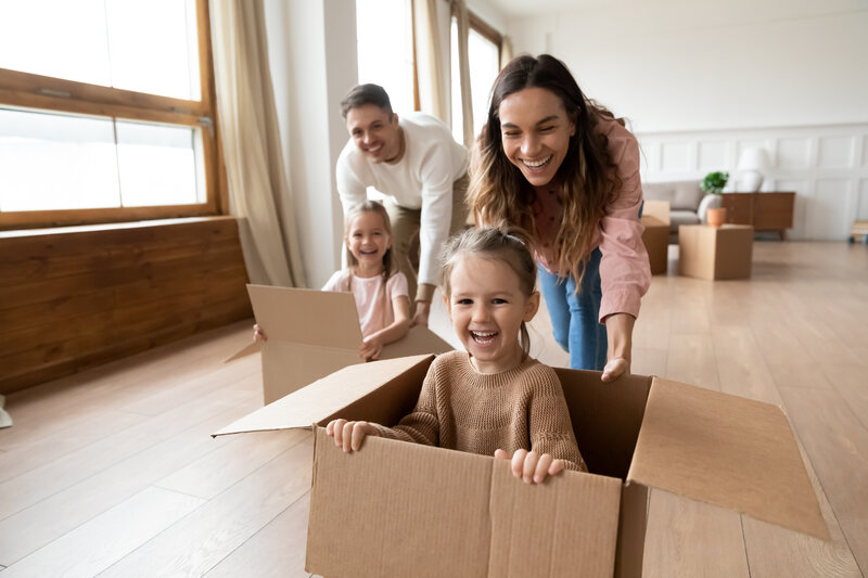 photo of mom and dad pushing two small children around in moving boxes
