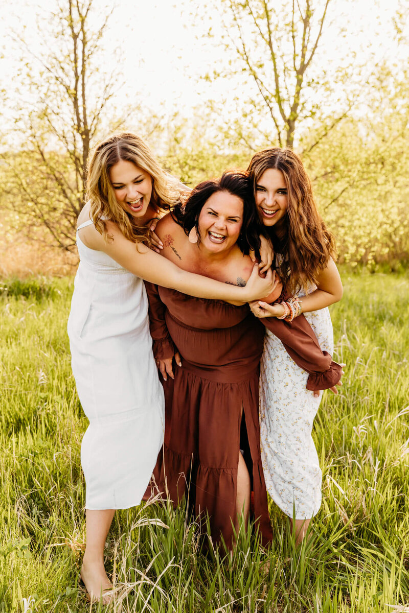daughters chasing mom in a field at sunset during family photo session