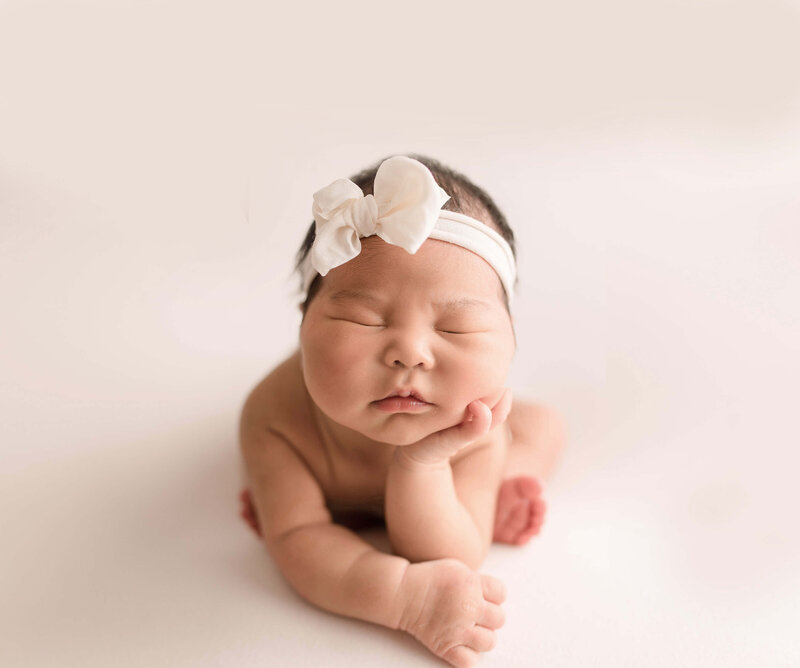 Newborn baby girl with bow holding head up with her hand