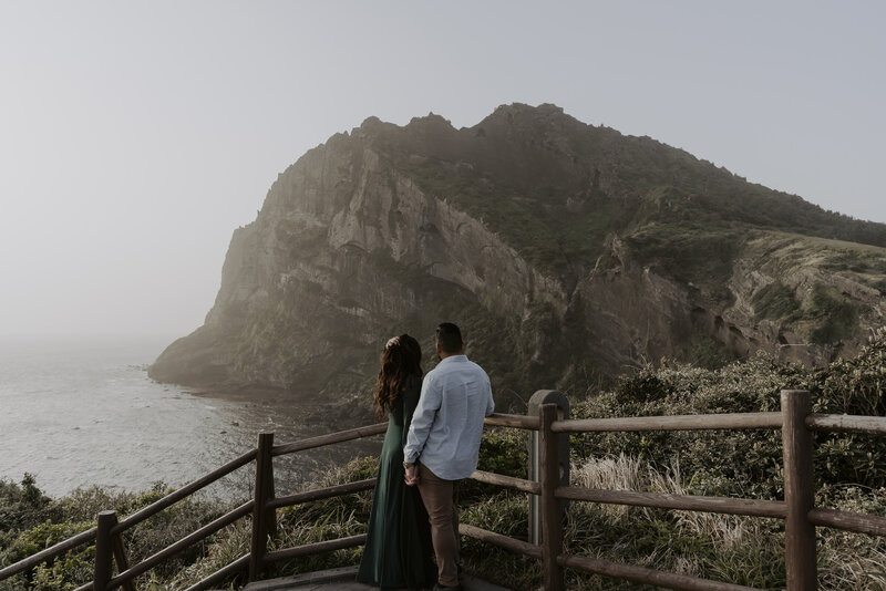 a couple hold hands and look at Seongsan Ilchulbong at sunrise in Jeju Island