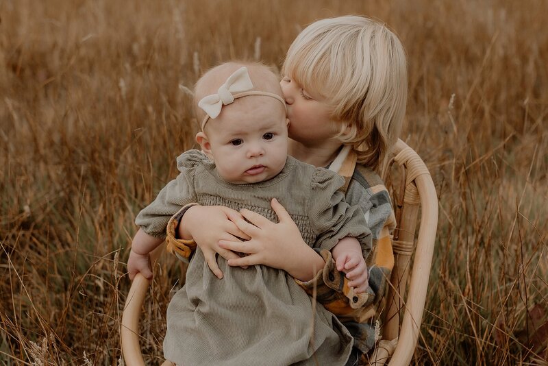 Two children hugging in a wicker chair in a field.