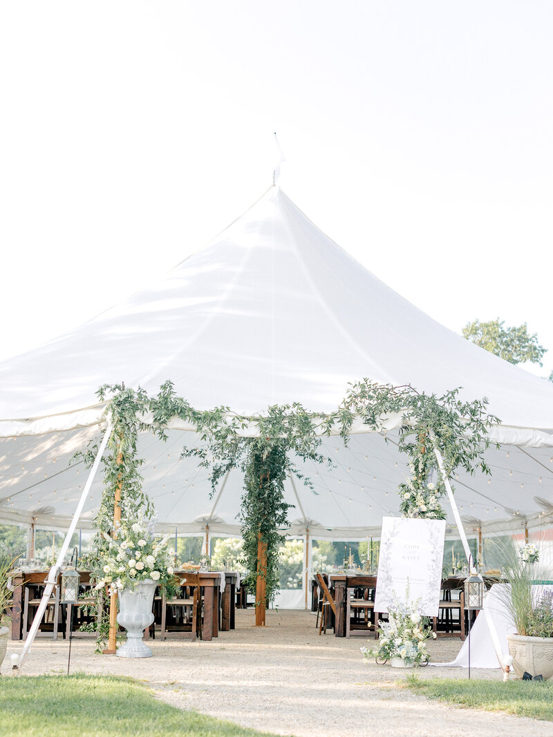 Outdoor shot of a wedding reception tent with greenery draped on it and tables underneath
