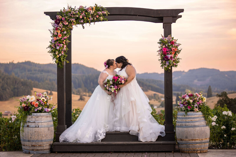 Brides kissing with sunset in background and floral installations and arrangements around them