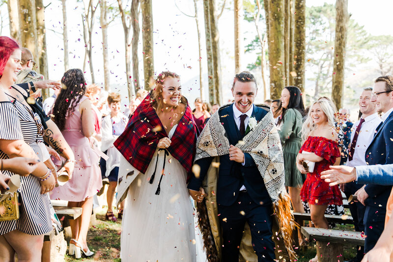 bride and groom walking under confetti in forest