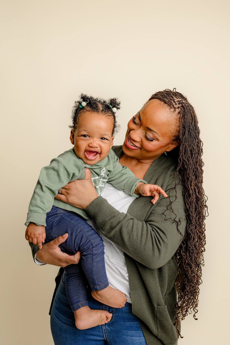 mom holds her daughter up next to her face smiling as she looks toward her