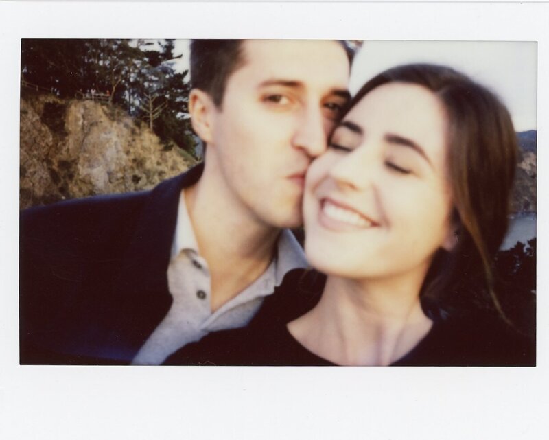 Polaroid of couple taking selfie. Man is kissing woman on cheek.