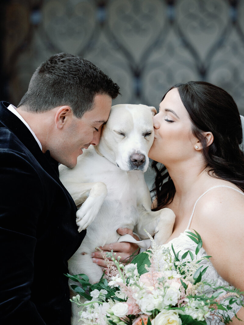A bride and groom standing with their beloved dog on their wedding day