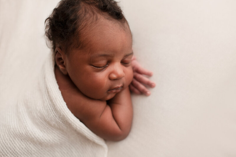 black newborn baby sleeping with head on hands with white background