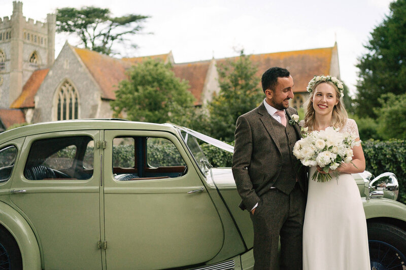 A bride and groom outside a church with a vintage car