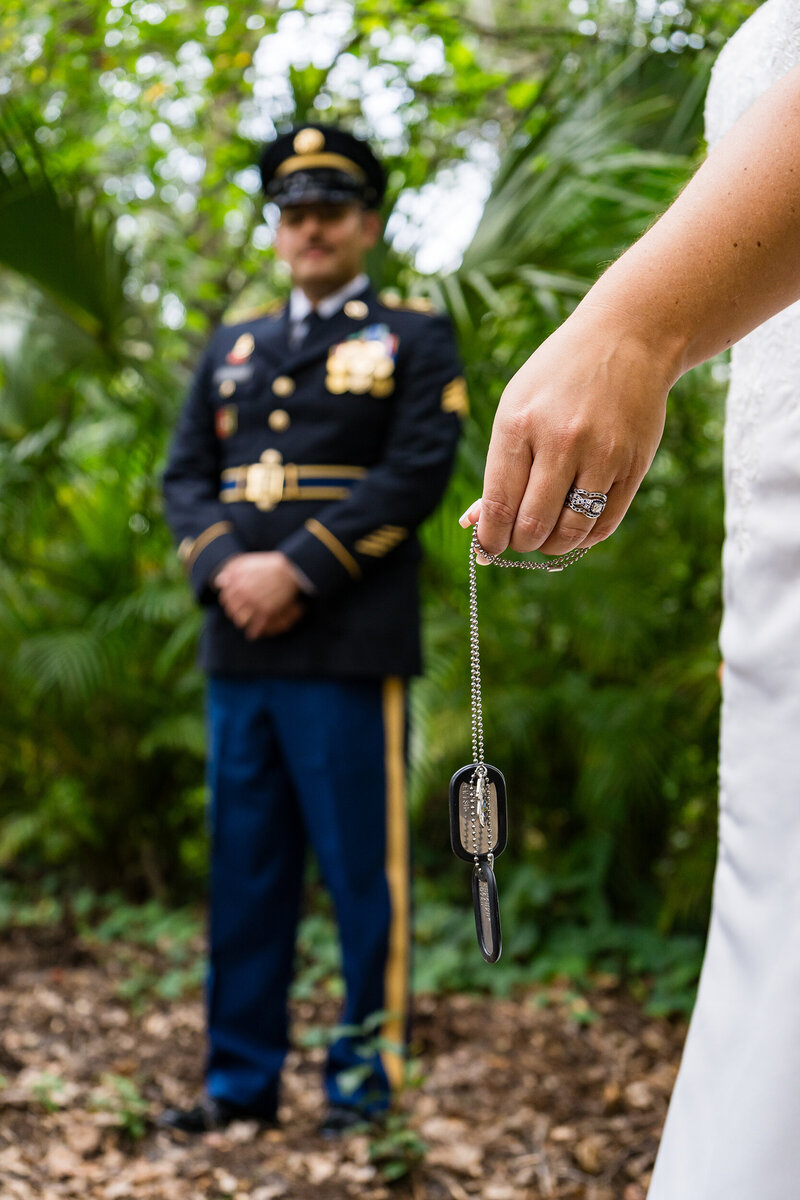 Bride holding her groom’s Army dog tags with the groom standing in uniform behind her during an emotional military wedding portrait in Colorado.
