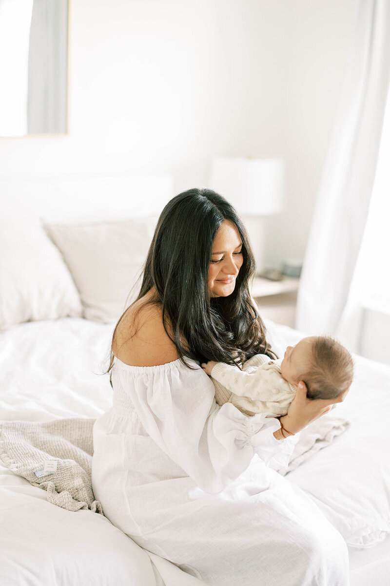 Mom holds baby in her arms in light and airy nursery for newborn photos.