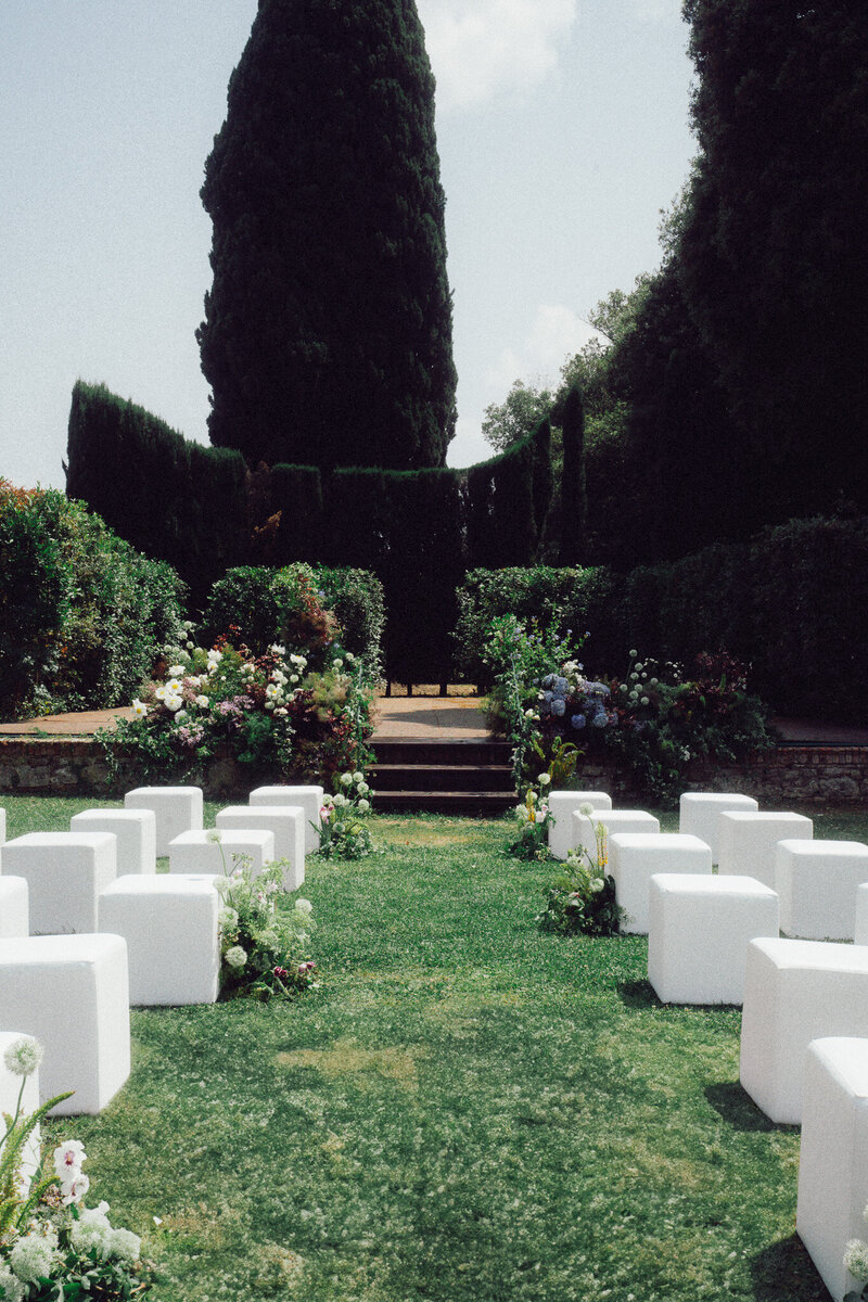 Elegant outdoor wedding ceremony setup in an Italian garden with modern white seating and lush florals, captured in a romantic, cinematic style by a luxury destination wedding photographer UK.