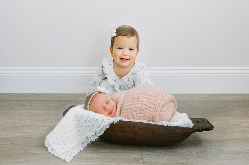 A toddler and her newborn baby sister both smiling at the camera