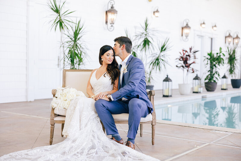 Bride and groom, sitting on a styled bench embracing on their wedding day.