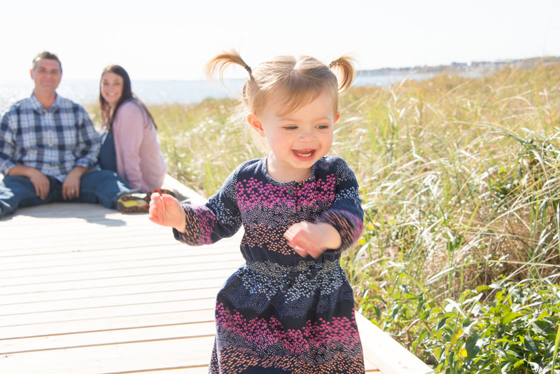 Embrace the spontaneity of childhood with Lorie-Lyn Photography's family beach sessions in Massachusetts. This vibrant image captures the essence of family joy, featuring a toddler's playful spirit with her parents fondly looking on in the background. Specializing in natural light and candid moments, Lorie-Lyn Photography ensures your family's story is told authentically and memorably.